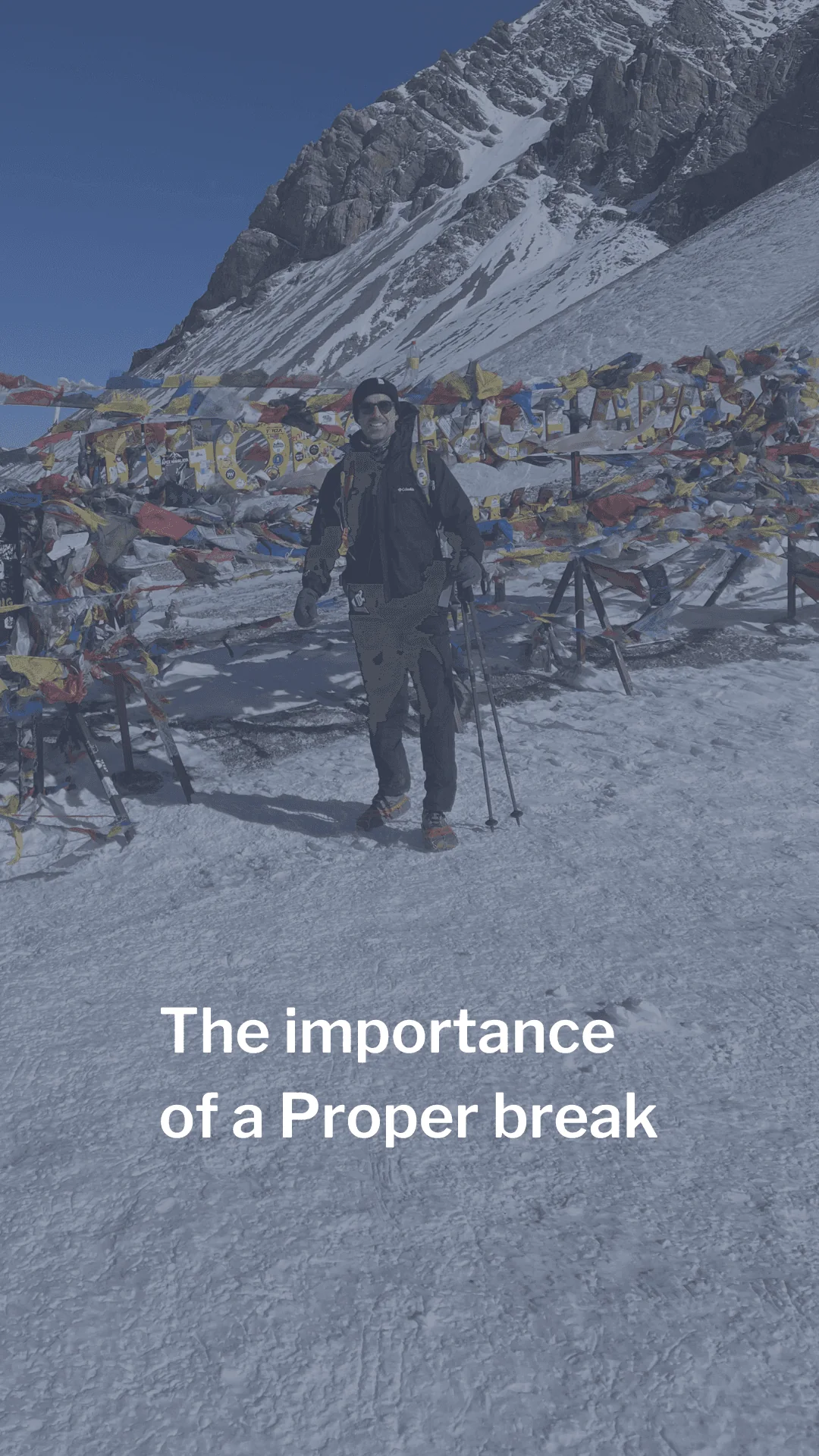 A hiker at a snowy mountain pass hung with prayer flags. Caption: The importance of a Proper break.